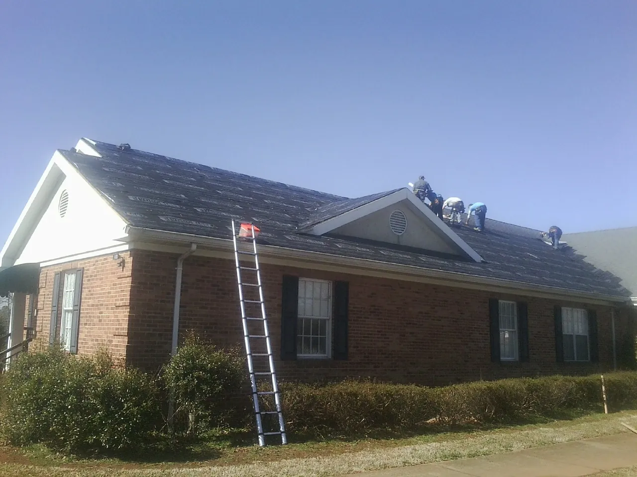 Crew tearing shingles off a brick ranch roof with a ladder set — Emergency Roof Repair work by our crew in Marietta